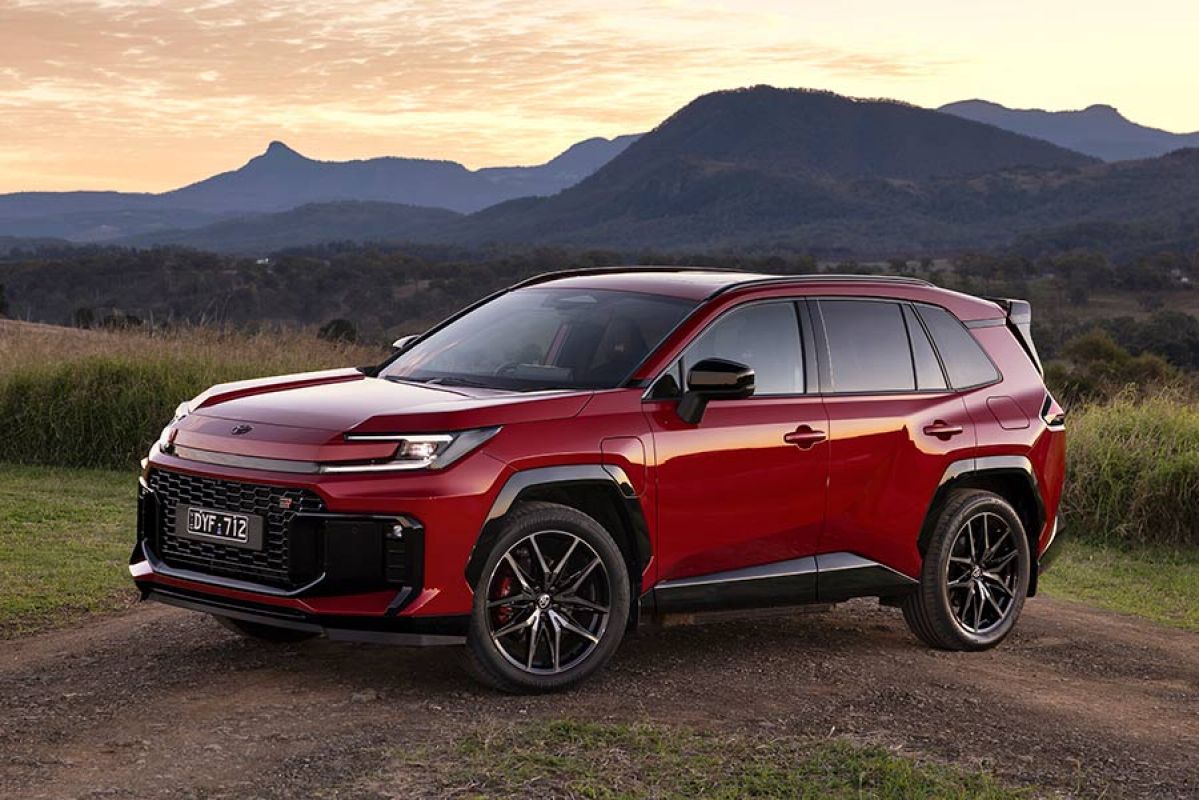 Red Toyota RAV4 GR Sport PHEV medium SUV parked across dirt track at base of mountain range at dusk.