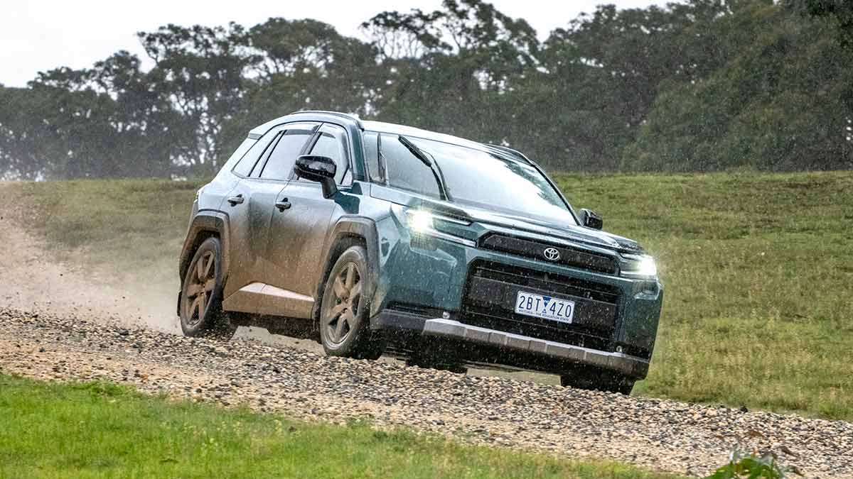 Metallic green Toyota RAV4 Edge SUV driving in rain on rocky gravel dirt road.