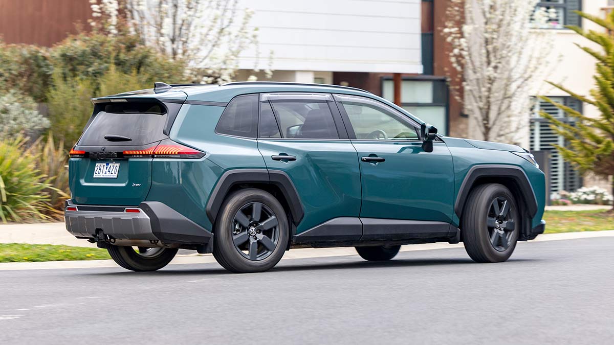 Rear view of metallic green Toyota RAV4 Edge SUV turning left on suburban street.