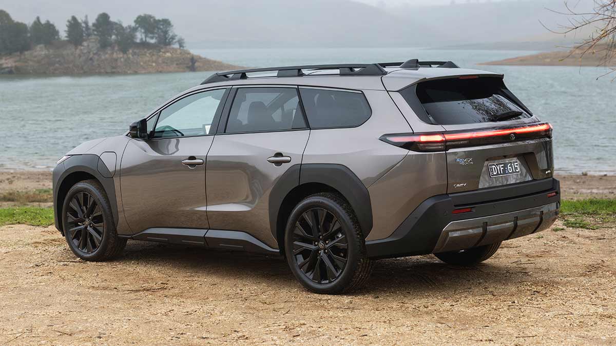 Rear view of bronze Toyota bZ4X Touring SUV parked on gravel in front of large waterway and headlands.