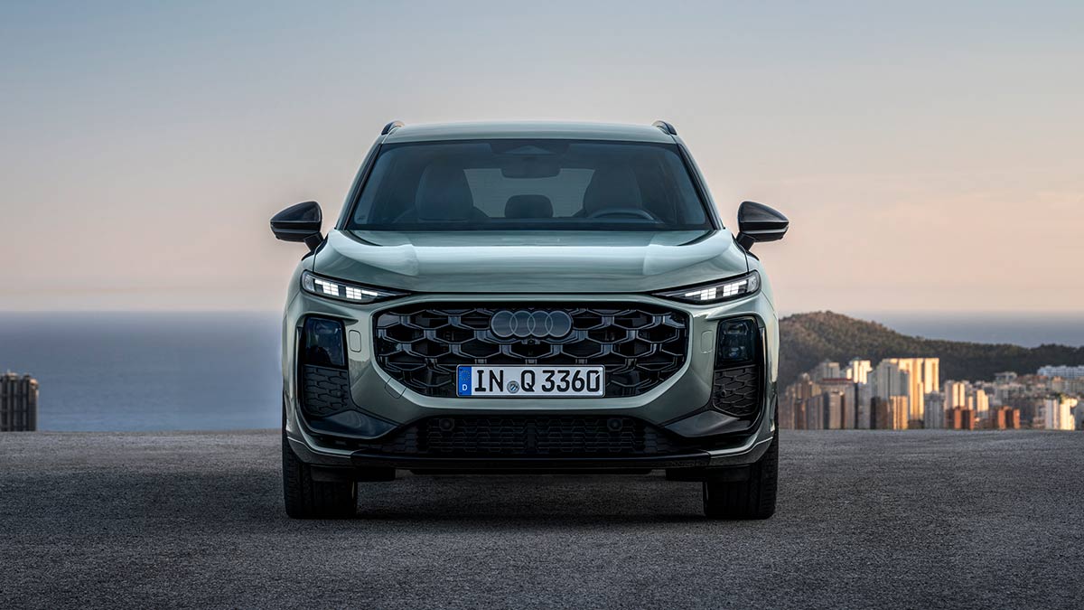 Front-on view of sage green metallic Audi Q3 small SUV at dusk in Europe overlooking mountain range, city and sea.
