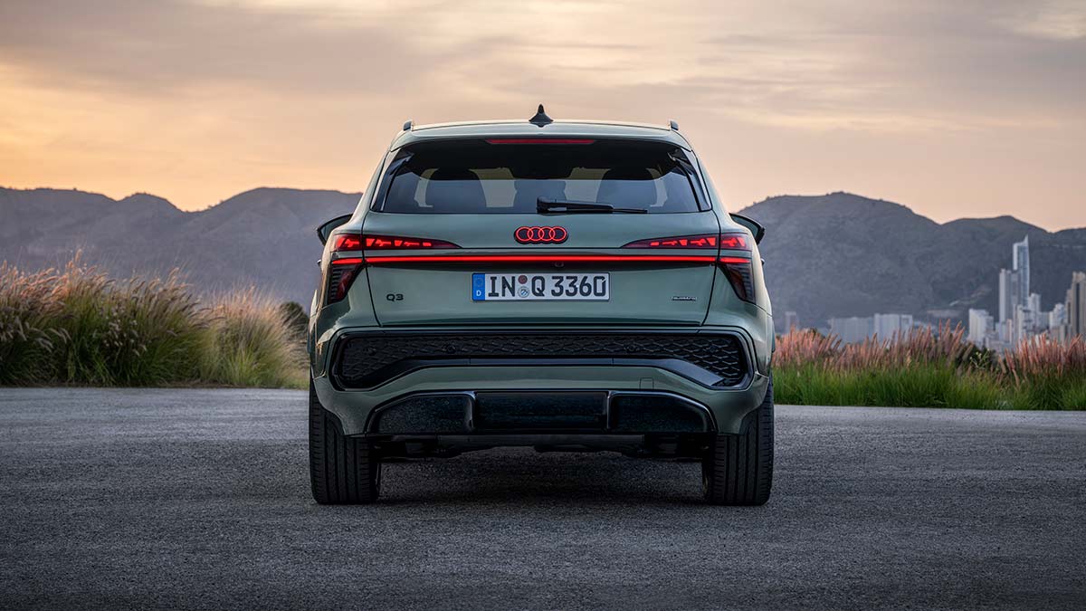 Rear view of sage green metallic Audi Q3 small SUV at dusk in Europe overlooking mountain range and city.