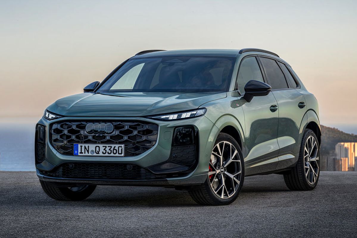 Sage green metallic Audi Q3 small SUV at dusk on coastline in Europe overlooking mountain, city and sea.