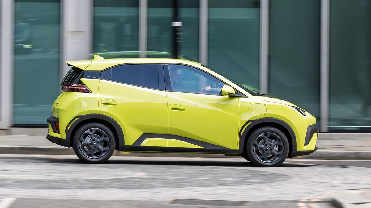 Lime green BYD Atto 1 EV hatch driving in front of green glass building.