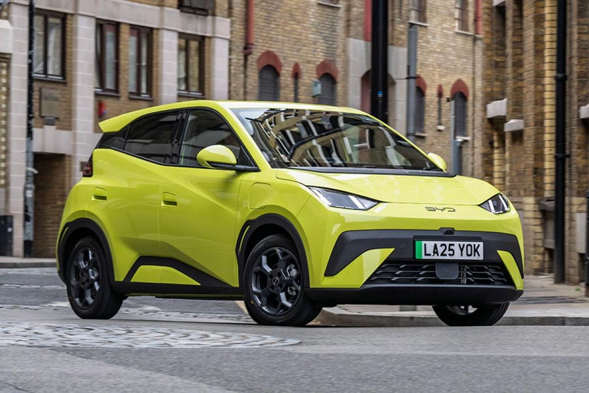 Lime green BYD Atto 1 EV hatch in UK city street surrounded by brown brick buildings.
