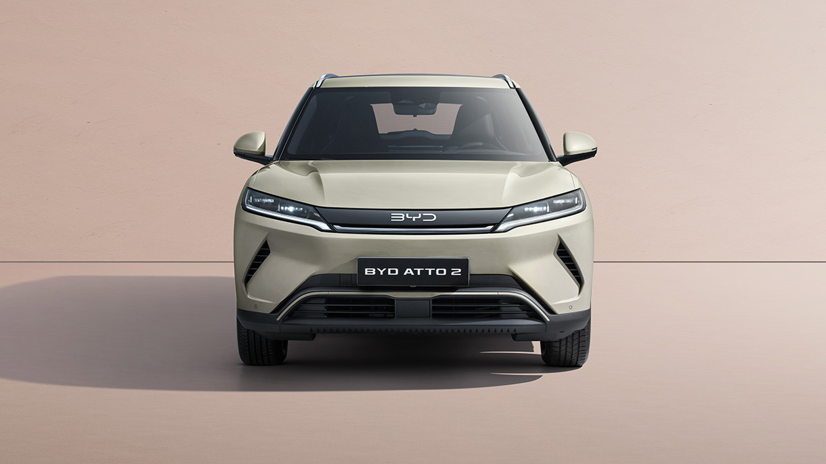 Front-on studio shot of light grey BYD Atto 2 small electric SUV with pastel tan background