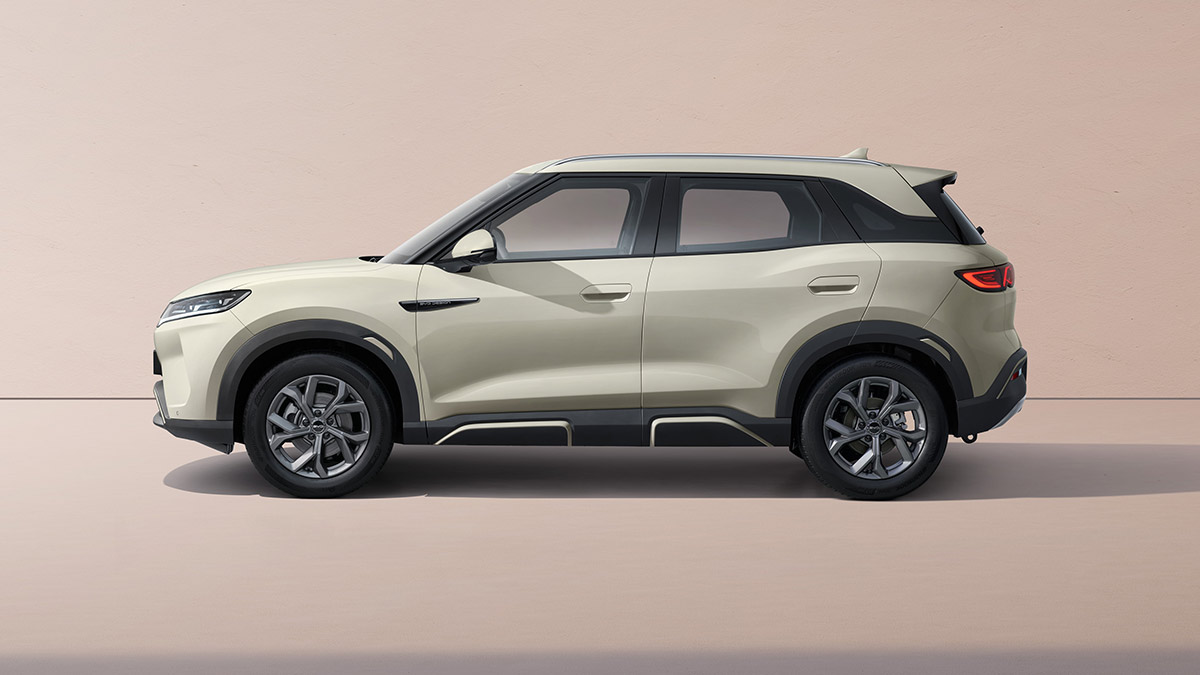 Side-on studio shot of light grey BYD Atto 2 small electric SUV with pastel tan background