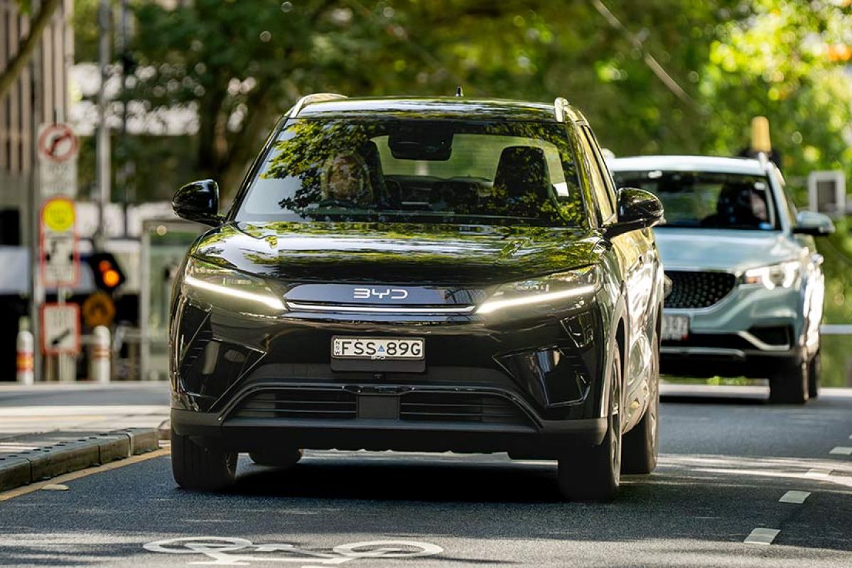 Black BYD Atto 2 electric small SUV driving on leafy street next to tram lines in Melbourne CBD.