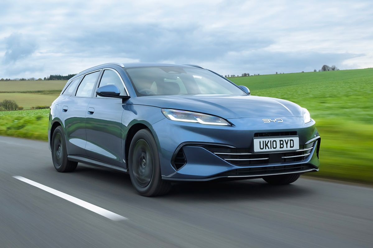Blue metallic BYD Seal 6 plug-in hybrid station wagon driving through lush green countryside in England.