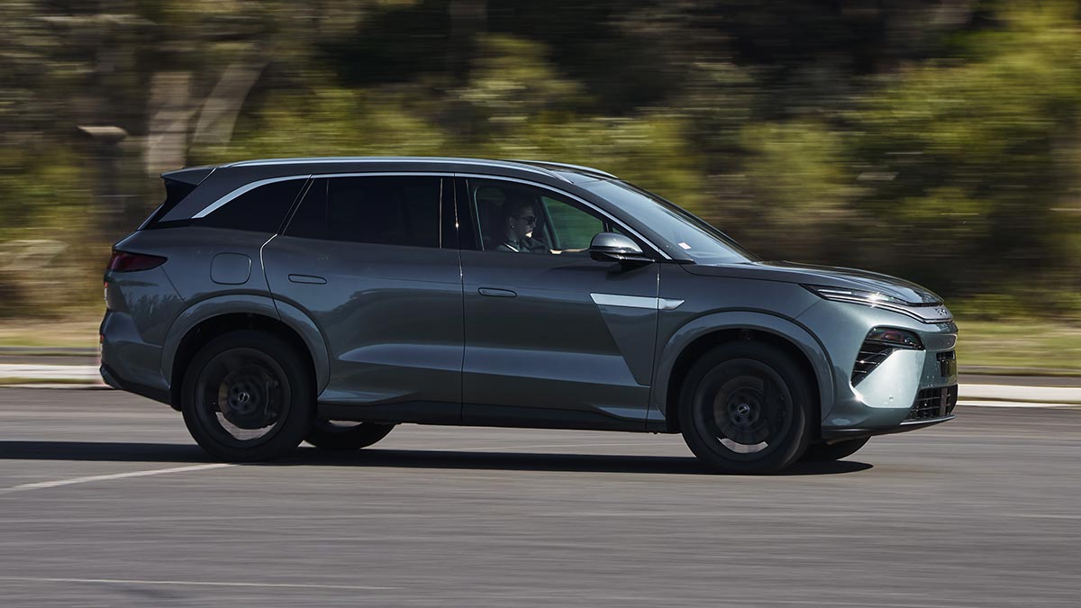 Side-on action shot of BYD Sealion 8 SUV in dark aquamarine metallic colour driving at bushy Lang Lang proving ground in regional Victoria.