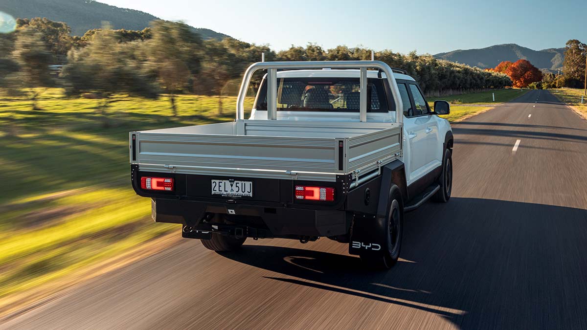 Rear view of white BYD Shark 6 Cab Chassis dual cab ute on tree-lined bitumen road approaching high country.