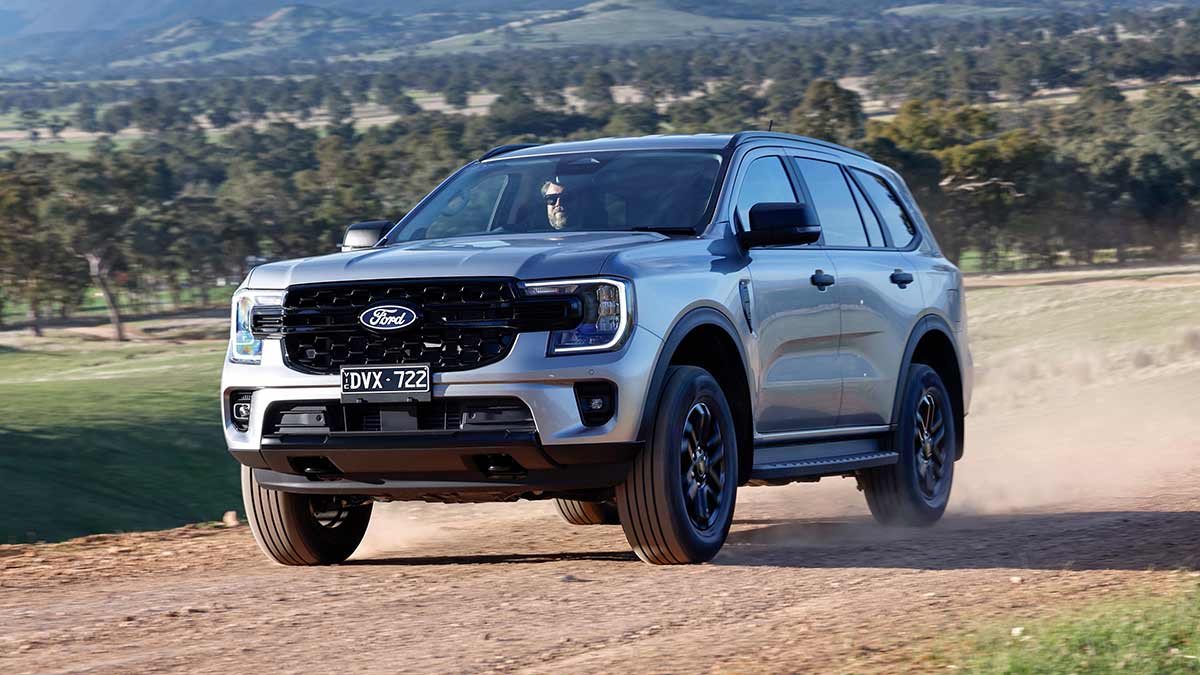 Silver metallic Ford Everest SUV driving on gravel road with panoramic rural view of rural behind.