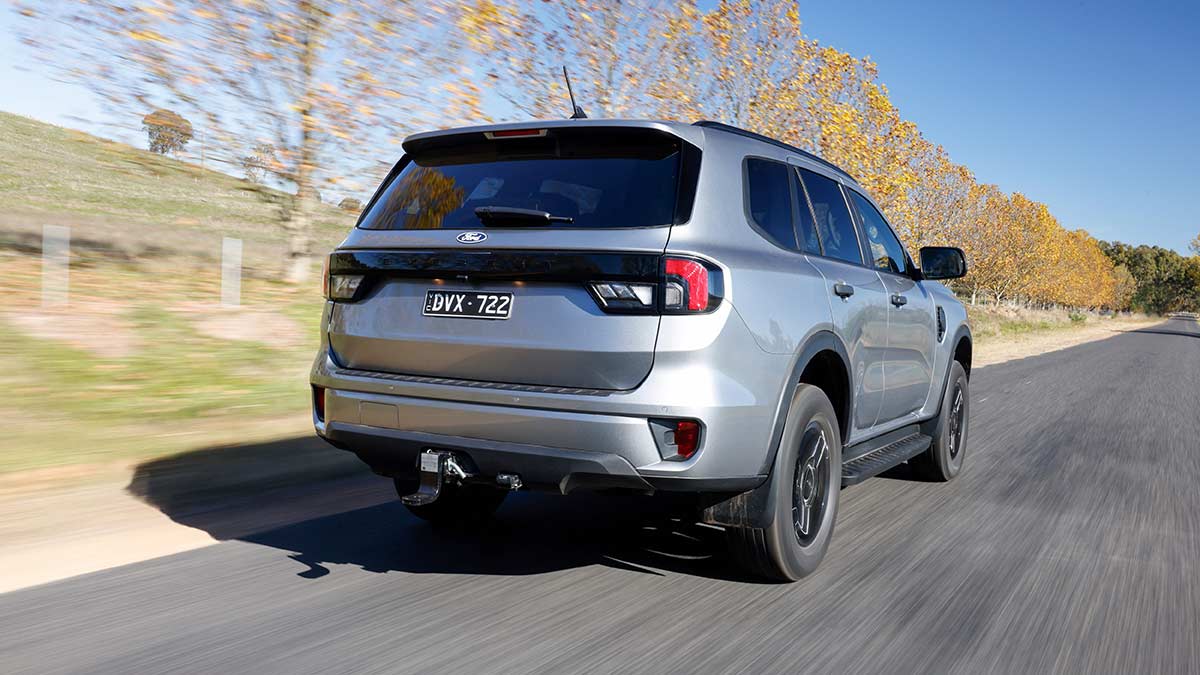 Rear view of silver metallic Ford Everest SUV driving on bitumen road lined with yellow leaved autumn trees.