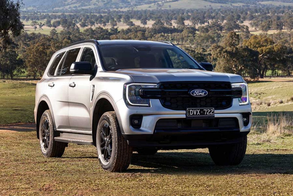 Silver metallic Ford Everest SUV on hillside of rural property with gravel road, paddocks and bush behind.