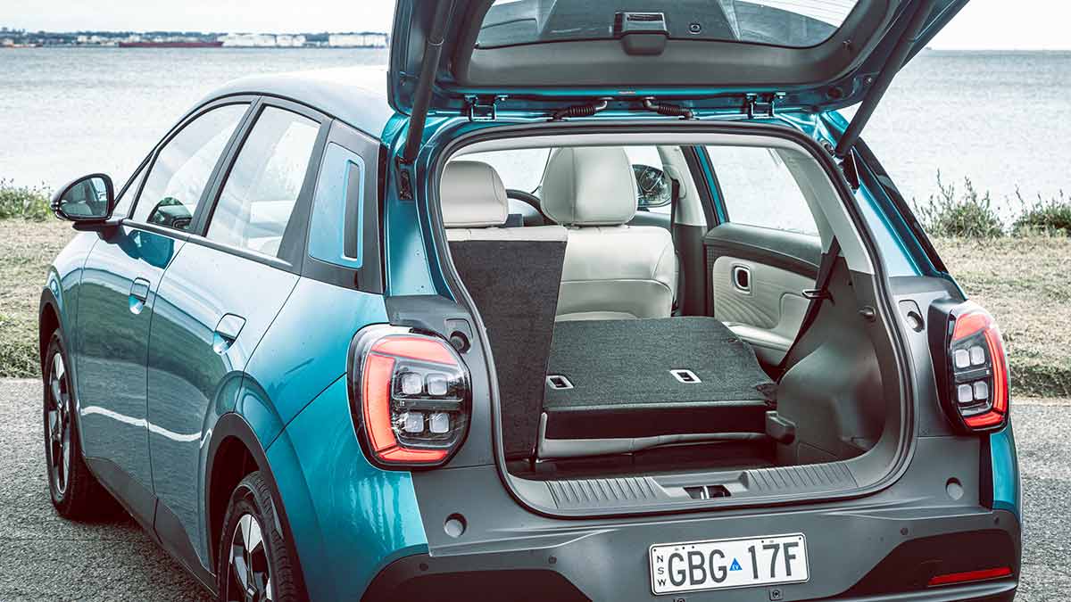 Rear view of GAC Aion UT parked at waterfront location with tailgate open and rear bench seat folded down to extend cargo area.