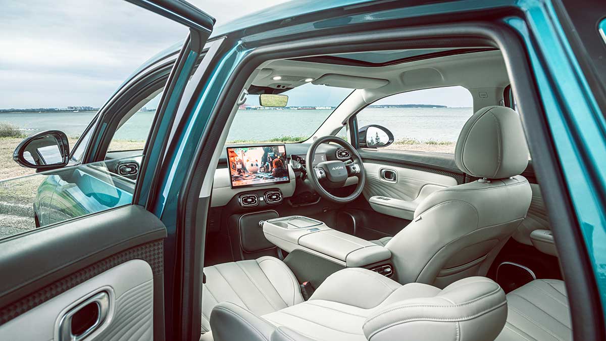 View inside cabin of GAC Aion UT Luxury EV parked at waterfront location, showing cream coloured trim and large dash screen.