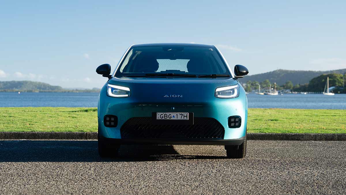 Front-on view of green GAC Aion UT electric hatch at waterfront carpark with yachts on bay in background.