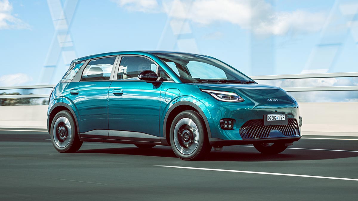 Green GAC Aion UT EV driving on bridge in urban area with concrete bollards and blue sky behind.