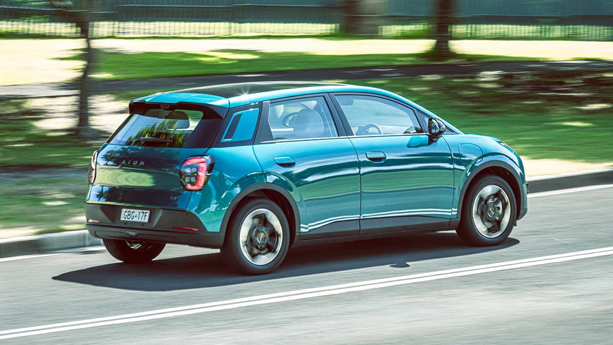 Rear action shot of green-blue GAC Aion UT electric hatch on leafy green suburban road.