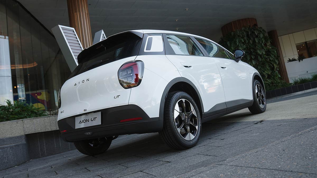 Rear view of white GAC Aion UT electric hatchback in front of modern apartment building.