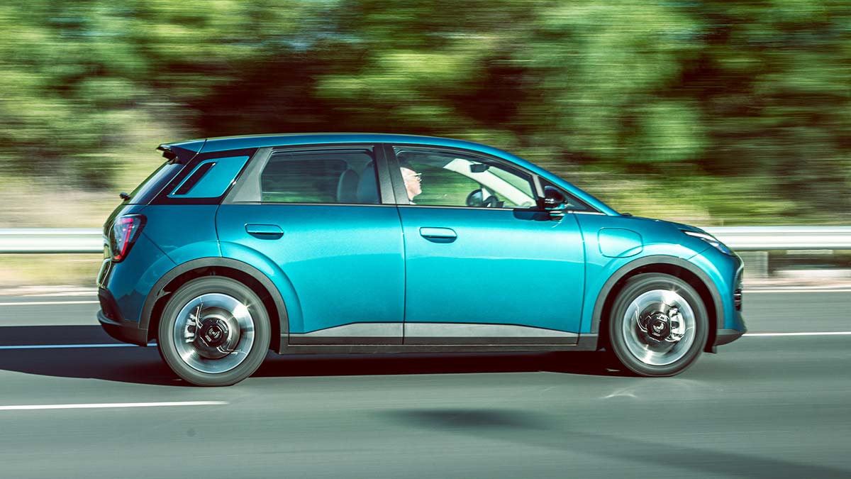 Side-on action shot of green GAC Aion UT electric hatch on road with green shrubbery blurred behind.