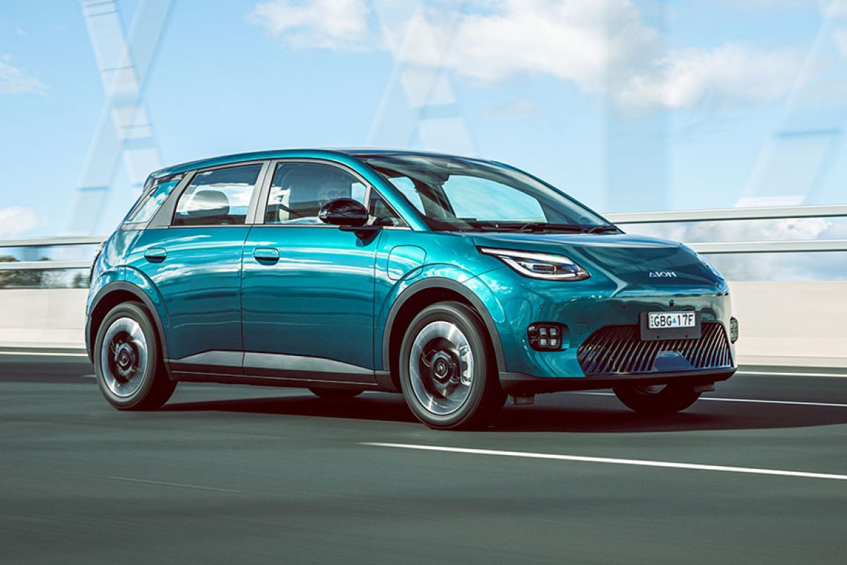 Green GAC Aion UT EV driving on bridge in urban area with concrete barrier and blue sky and white clouds behind.