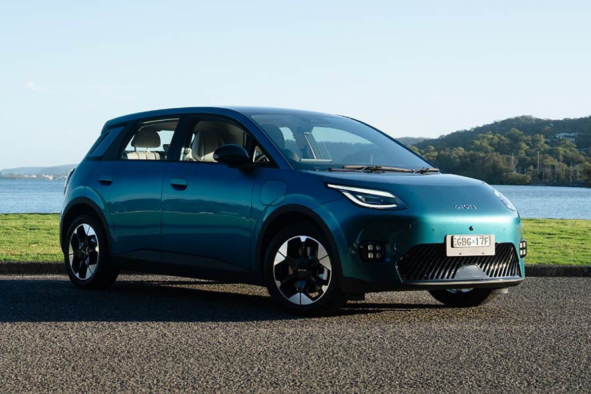 Green GAC Aion UT electric hatch at waterfront carpark with bay and bushland in background.