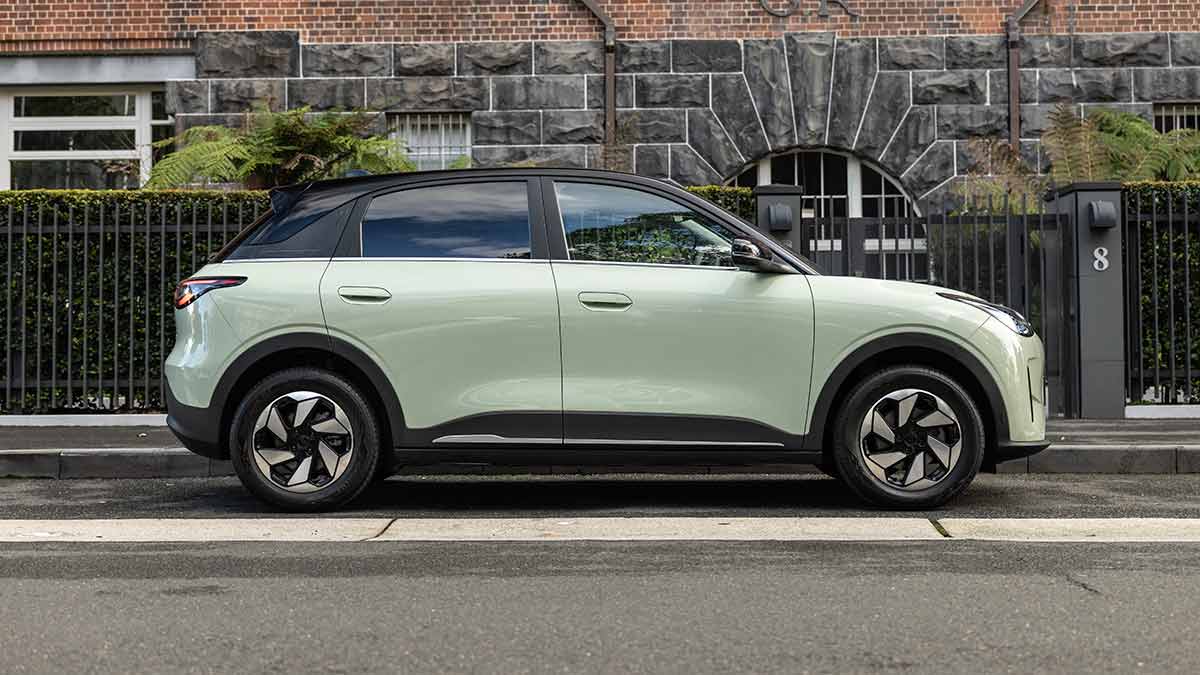 Profile shot of light green Geely EX2 EV hatch parked outside bluestone building with black fence.