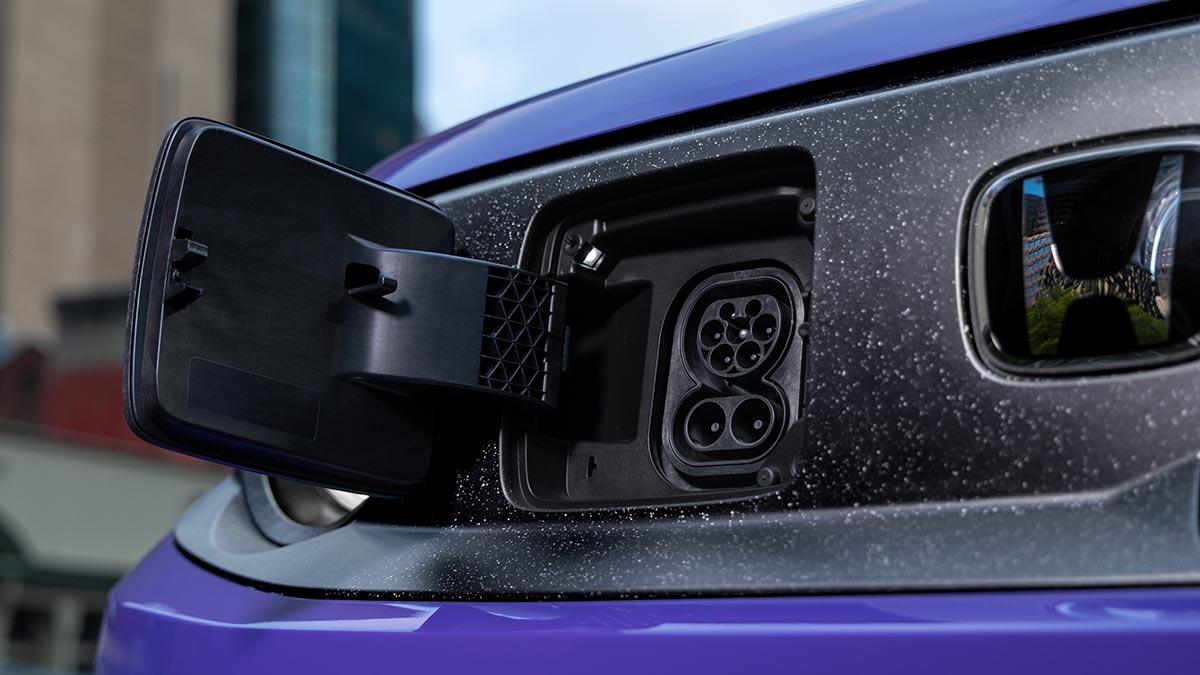 Charging flap open at front of purple Honda Super-One EV hatch showing AC and DC plugs.