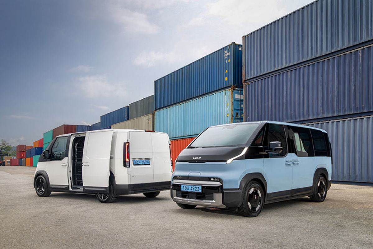 Blue Kia PV5 Passenger EV people-mover and white PV5 Cargo van in front of triple-stacked coloured shipping containers.