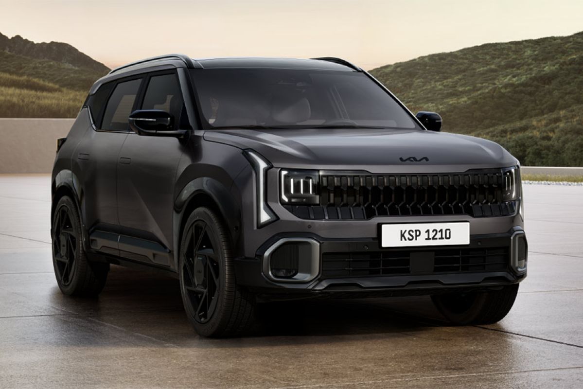 Dark grey Kia Seltos X-Line SUV parked on large concrete forecourt in front of green highland mountains.