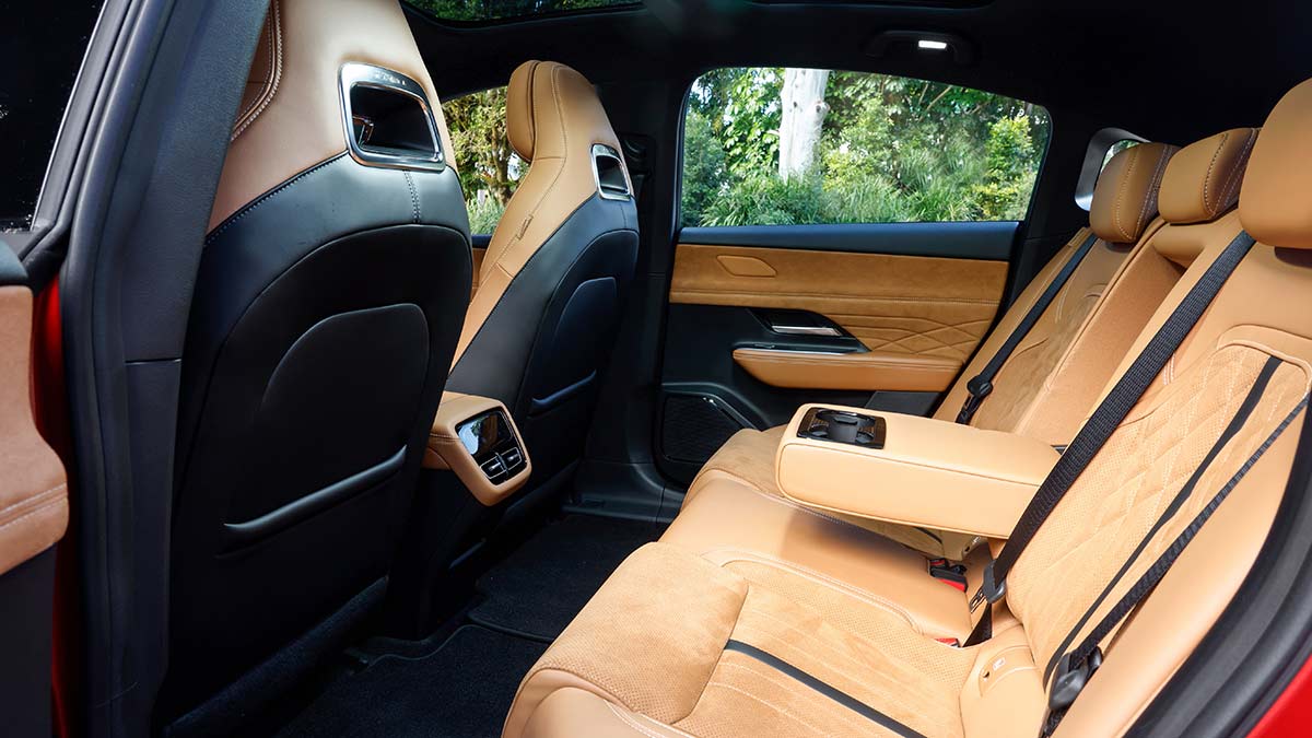 Rear seat area of Mazda 6e electric sedan pictured from rear left door, showing tan seat trim and pull-down centre armrest.