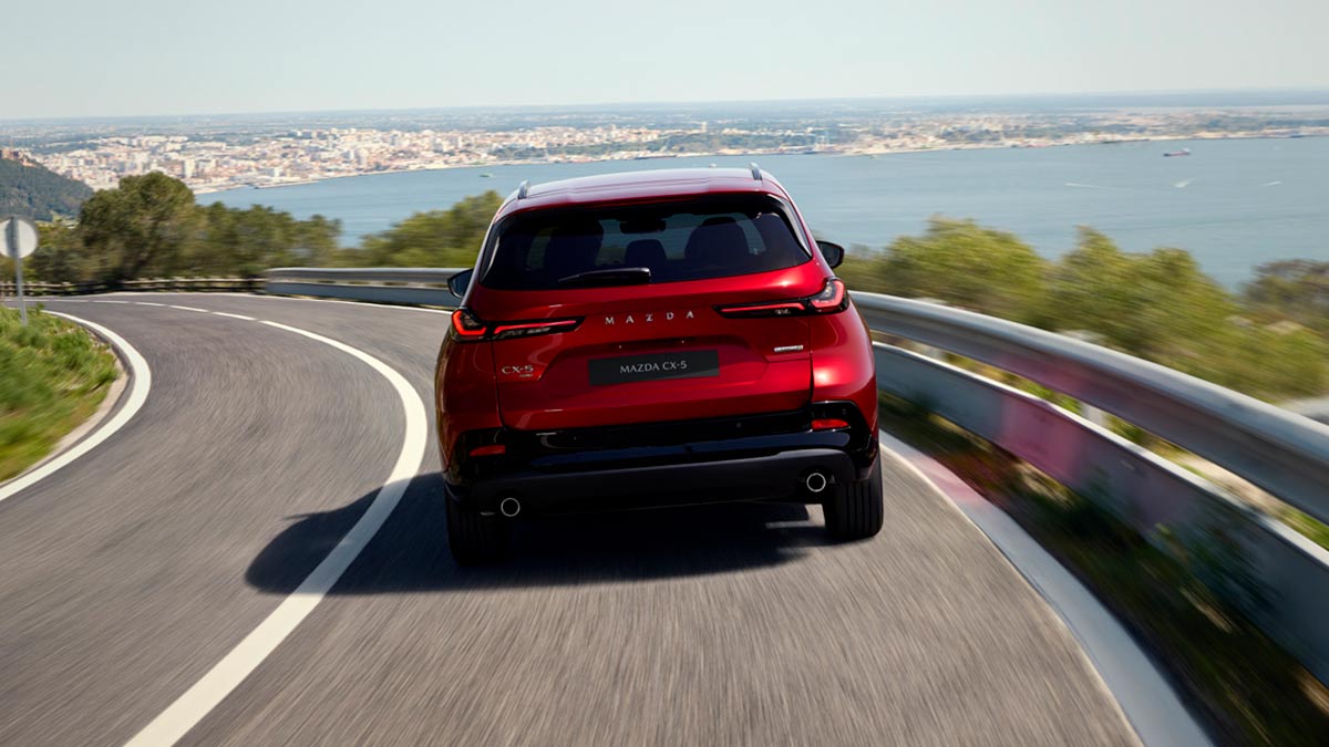 Rear-end view of red Mazda CX-5 SUV on coastal road.