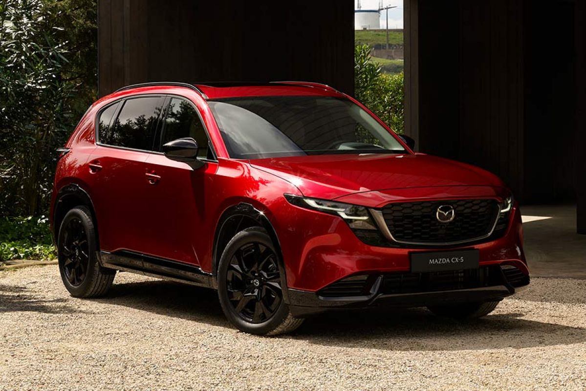 Red Mazda CX-5 medium SUV parked outside dark timber-cladded building.