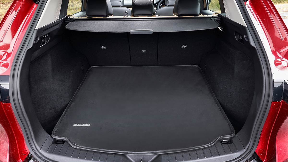 Tailgate of red Mazda CX-5 SUV open, showing large boot area behind three-way split-fold rear seats.