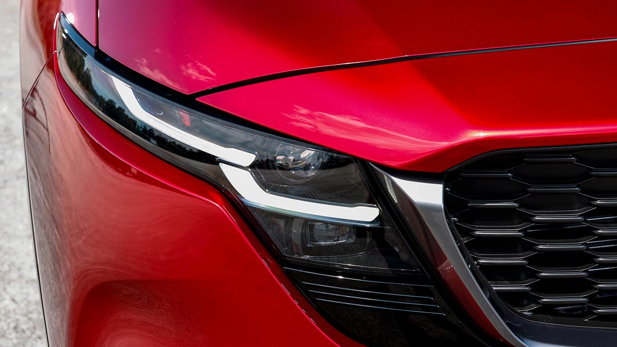 Narrow, angular LED headlight detail at front of red Mazda CX-5 SUV.