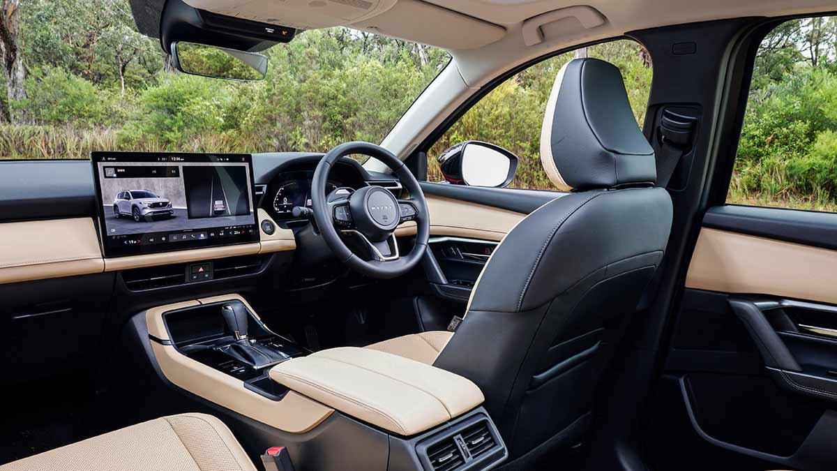 View of driver’s area in Mazda CX-5 Akera SUV from back seat, showing tan leather upholstery and minimalist layout with large central screen.