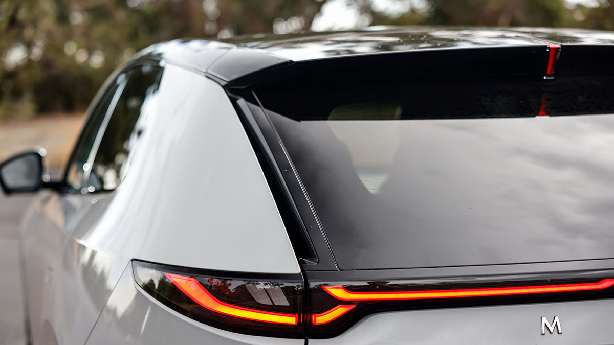 Left rear corner of white Mazda CX-6e SUV with thin LED tail-light strip and air vent behind pillar.