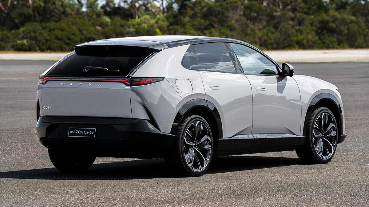 Rear view of LHD Euro-spec Mazda CX-6e SUV on forecourt with native bush behind at Lang Lang proving ground in Victoria.