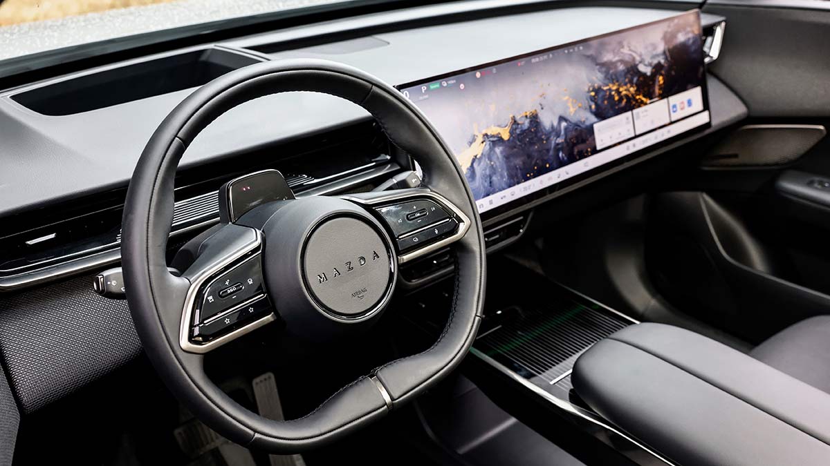 Sparse cockpit of Mazda CX-6e SUV with head-up display in lieu of instrument panel next to giant touchscreen across dash.