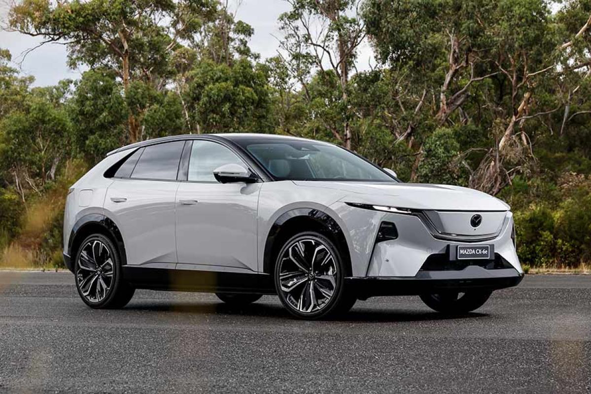 White LHD Euro-spec Mazda CX-6e SUV on forecourt with native bush behind at Lang Lang proving ground in Victoria.