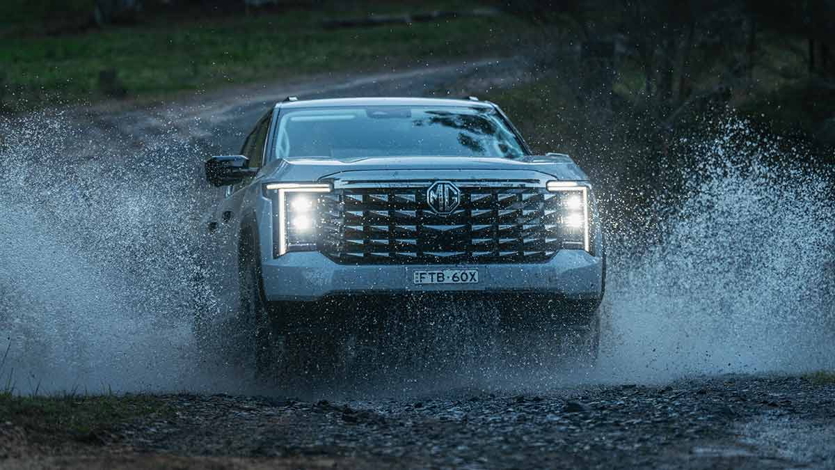 MG U9 ute driving through creek crossing with water splashing high at both sides of vehicle.