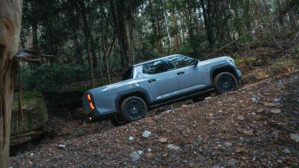 Blue MG U9 dual-cab ute driving up steep off-road track in bush.
