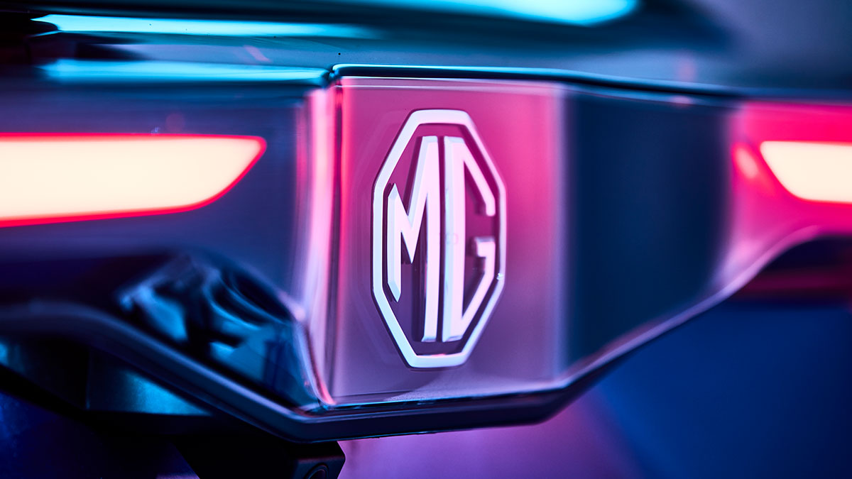 Close-up of MG badge on blue MG4 EV hatch at centre of rear light bar with red LEDs.
