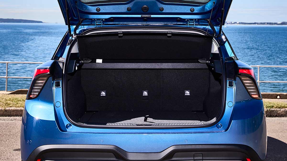 Tailgate open to show cargo area of blue MG4 electric hatchback parked at seafront location.