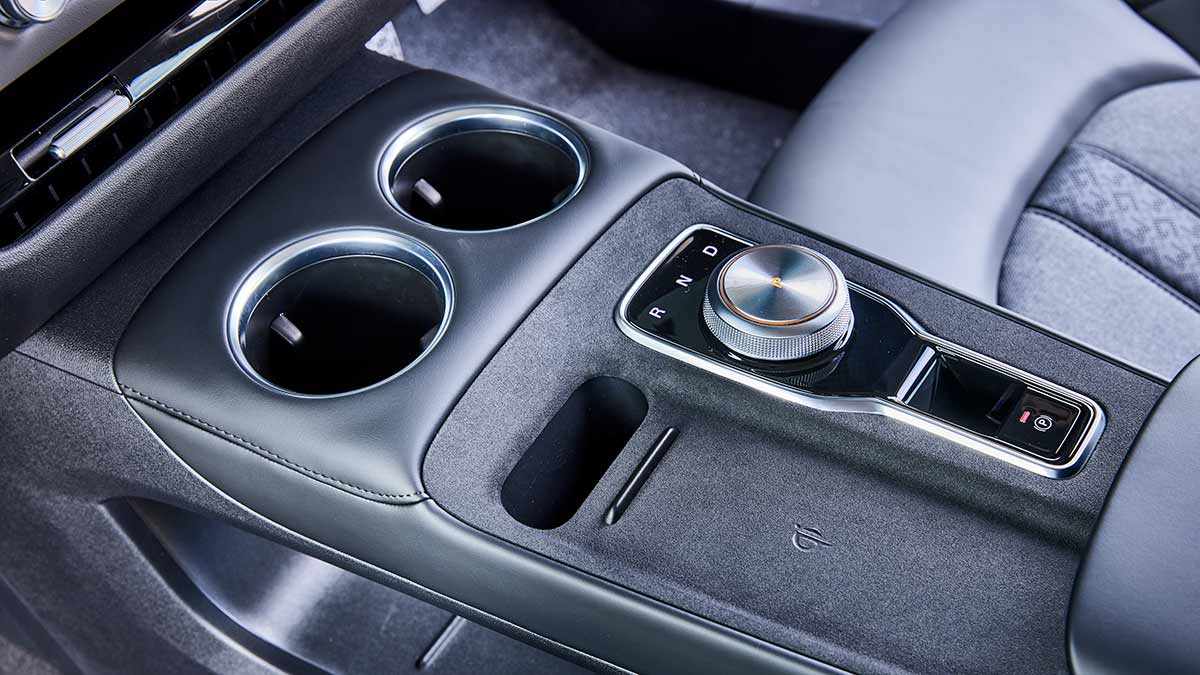 Centre console of MG4 EV with twin cupholders, rotary transmission selector and wireless phone charging pad.