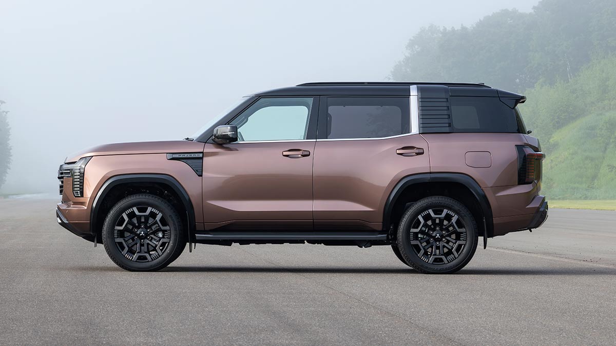 Side profile view of bronze Mitsubishi Pajero large seven-seater SUV with black roof in misty green forested location. 