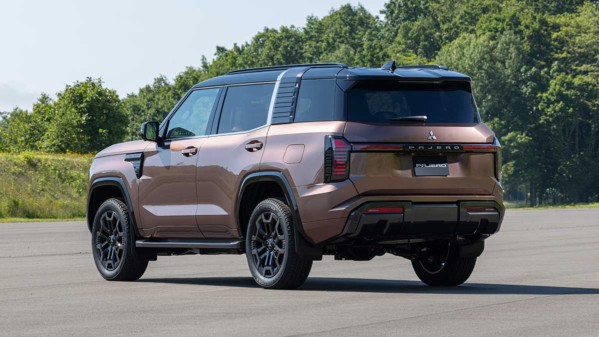 Rear view of bronze Mitsubishi Pajero SUV with black roof in open area at Thailand proving ground surrounded by forest.