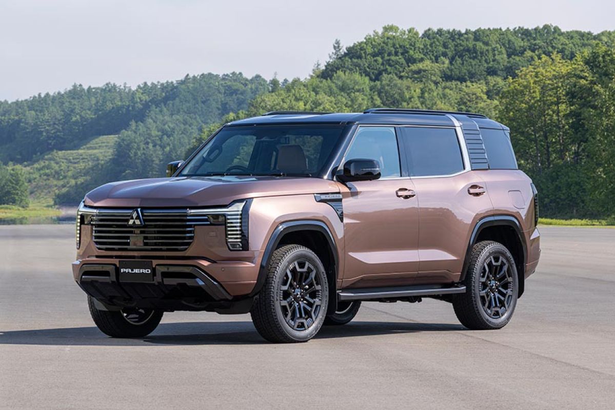 Bronze Mitsubishi Pajero SUV with black roof in open area at Thailand proving ground surrounded by forest.