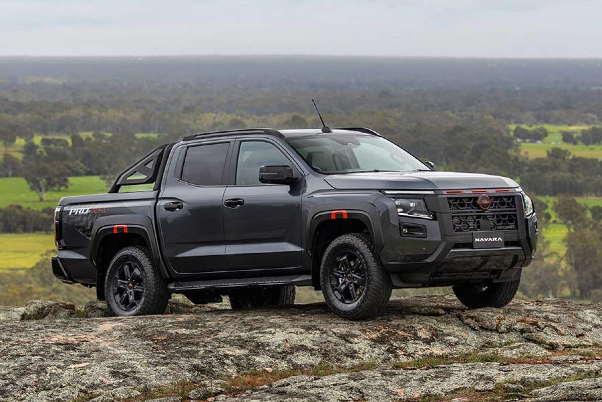 Dark grey Nissan Navara Pro-4X on rocky granite hilltop with lush green pastoral land and gum trees behind.